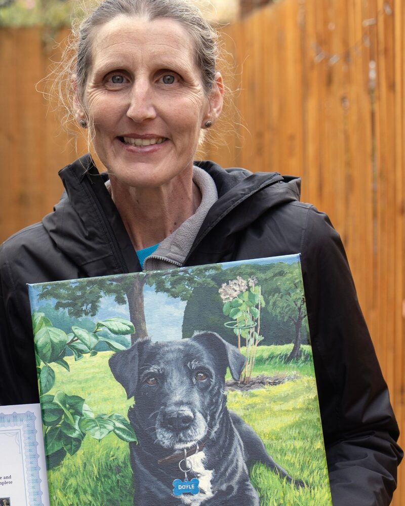 Rolo's owner holding the acrylic painting of Rolo in the garden